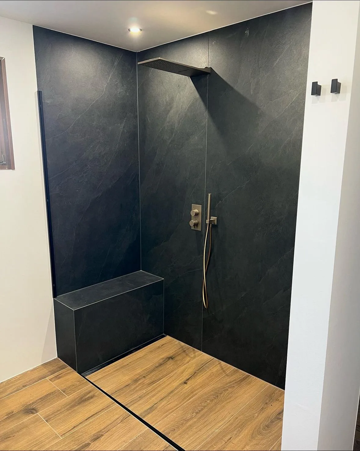 Bodengleiche Dusche mit schwarzen Wandplatten, Sitzbank und Boden in Holzoptik
