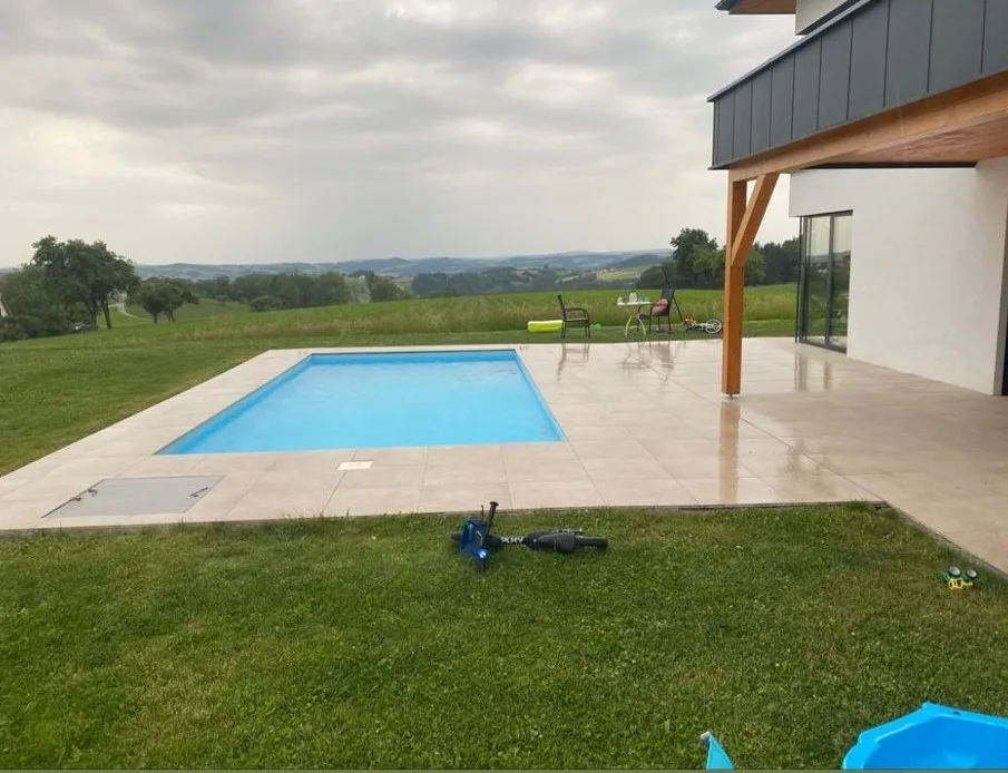 Terrasse mit hellen Platten rund um einen Pool, dahinter Wiesen