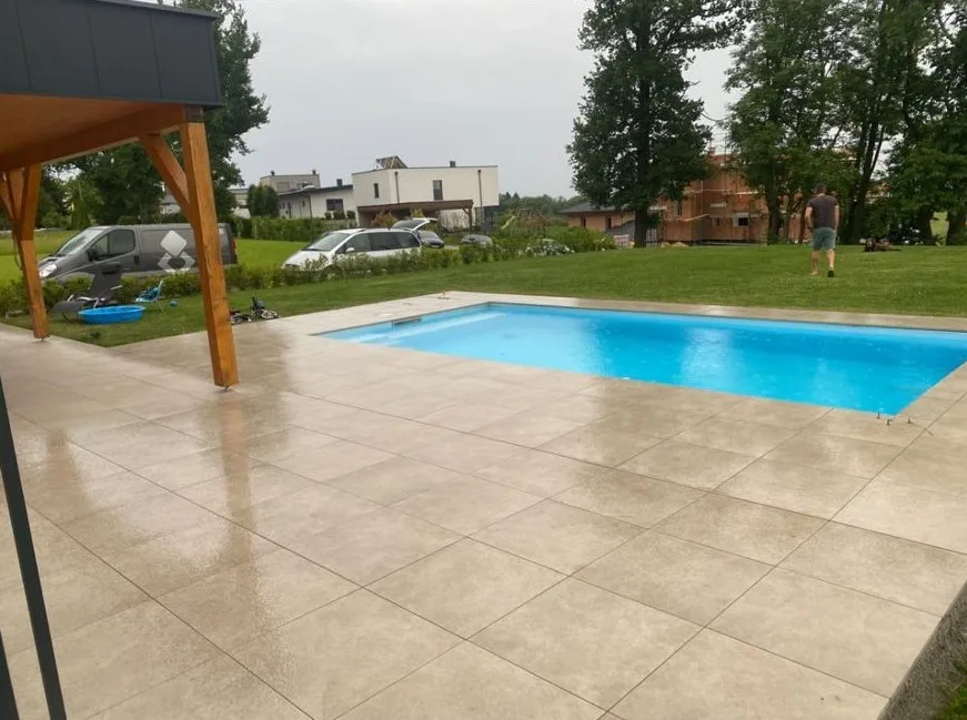 Poolterrasse mit großformatigen hellen Platten unter einem Vordach
