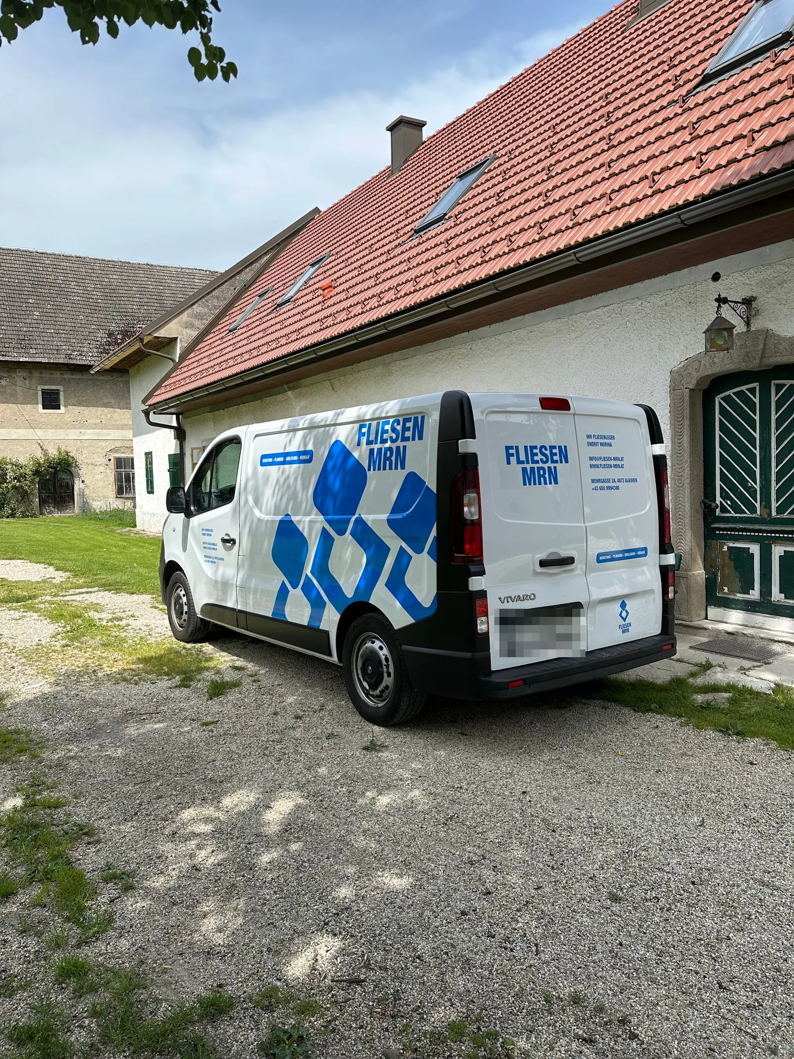 Weißer Firmenwagen mit blauer Beschriftung Fliesen MRN vor einem Bauernhaus